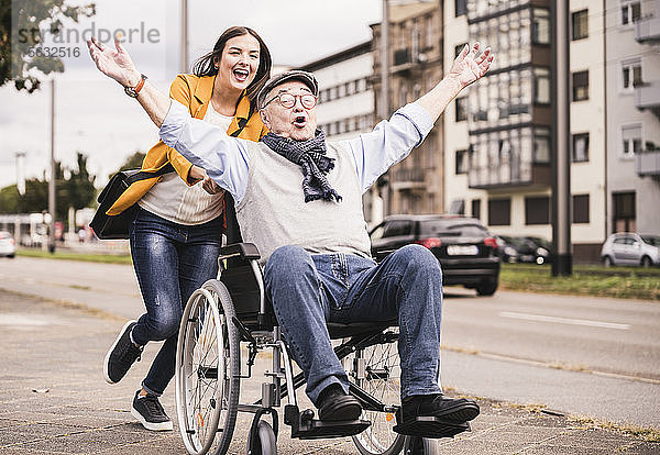 Porträt einer jungen Frau  die einen älteren Mann im Rollstuhl auf dem Bürgersteig schiebt