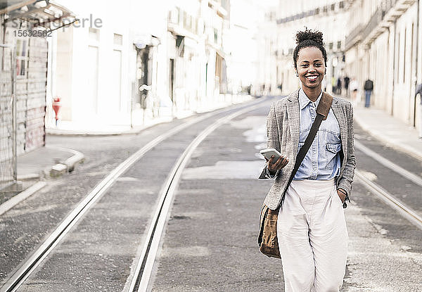 Lächelnde junge Frau mit Handy in der Stadt unterwegs  Lissabon  Portugal