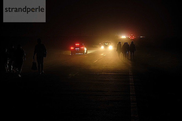 Portugal  Algarve  Autos passieren Silhouetten von vier Personen  die nachts auf der Straße in Cape Saint Vincent spazieren