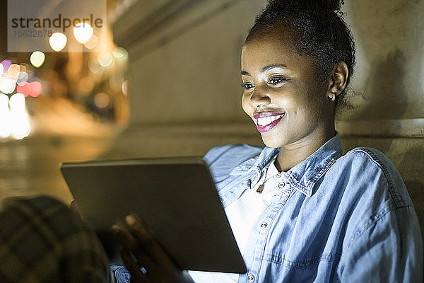 Portrait einer glücklichen jungen Frau mit digitalem Tablet in der Stadt bei Nacht  Lissabon  Portugal