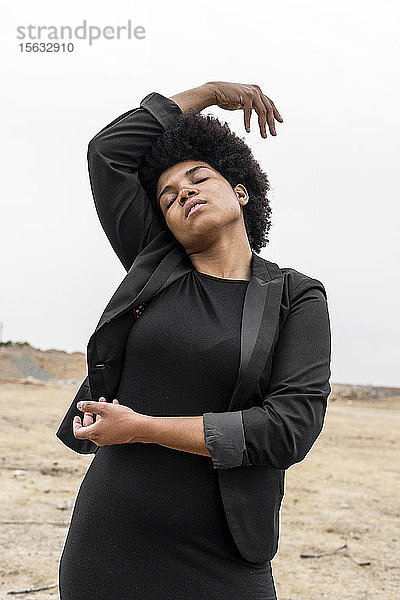 Porträt einer schwarz gekleideten jungen Frau  die in trostloser Landschaft auftritt