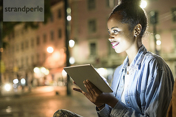 Porträt einer lächelnden jungen Frau mit digitalem Tablet in der Stadt bei Nacht  Lissabon  Portugal