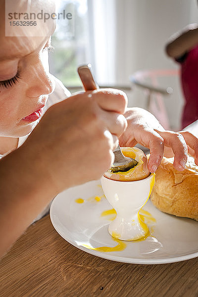 Mädchen isst ein gekochtes Ei am Esstisch