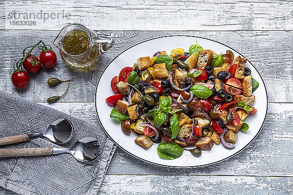 Panzanella  italienischer Brotsalat mit geröstetem Ciabatta  Tomaten  Oliven  roten Zwiebeln  Kapernäpfeln und Basilikum auf Teller