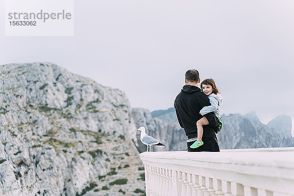 Porträt eines fröhlichen kleinen Mädchens auf dem Arm ihres Vaters beim Anblick  Cap Formentor  Mallorca  Spanien