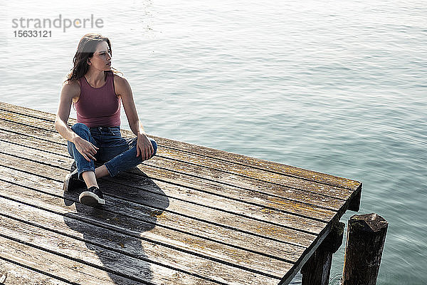 Junge Frau sitzt auf einem Steg und schaut in die Ferne  Starnberger See  Deutschland
