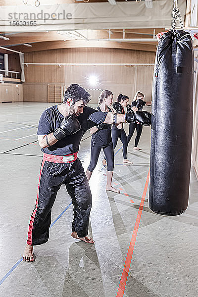 Trainer und Boxerinnen trainieren am Boxsack in der Sporthalle