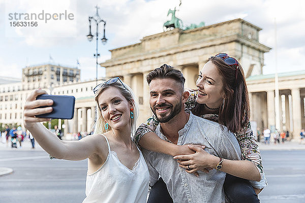 Porträt von drei Freunden  die sich mit dem Handy vor dem Brandenburger Tor in Berlin selbstständig machen