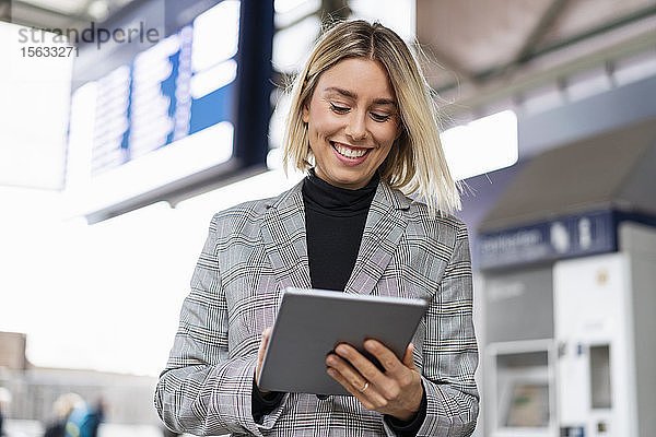 Lächelnde junge Geschäftsfrau mit Tablette am Bahnhof