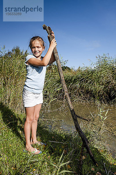 Porträt eines Mädchens mit einem Ast  das an einem Wasserlauf steht  Darß  Mecklenburg-Vorpommern  Deutschland