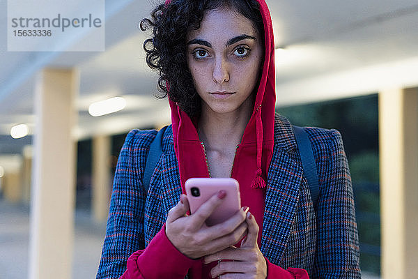 Porträt einer jungen Frau mit Mobiltelefon am Abend