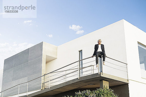 Geschäftsmann sitzt auf einem Geländer vor seinem modernen Haus