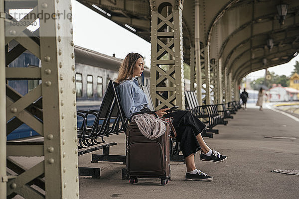 Junge weibliche Reisende wartet am Bahnhof und benutzt E-Book