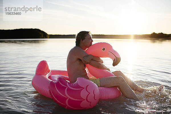 Junger Mann mit Flamingo-Pool schwimmt auf einem See