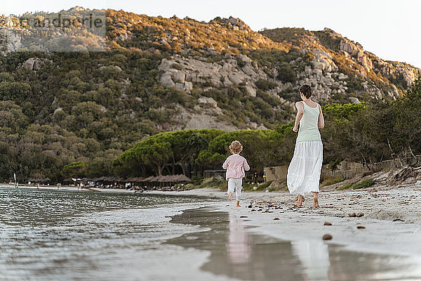 Rückansicht einer Mutter  die mit ihrer Tochter am Strand läuft