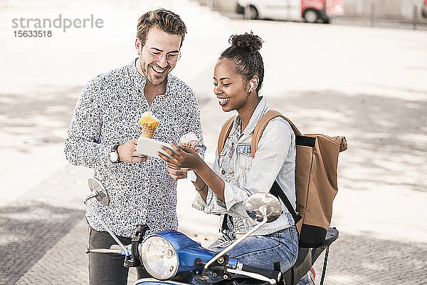 Glückliches junges Paar mit Motorroller und Eiscreme mit dem Handy in der Stadt  Lissabon  Portugal