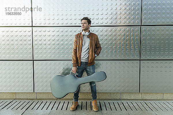 Mann mit Gitarre vor einer Silberwand stehend