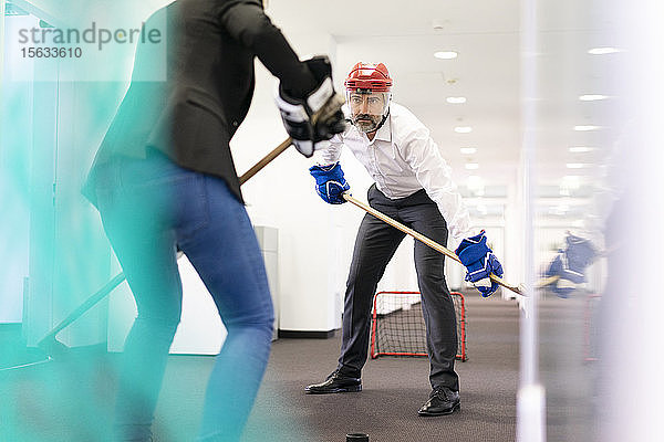 Geschäftsfrau und Geschäftsmann spielen Eishockey im Amt