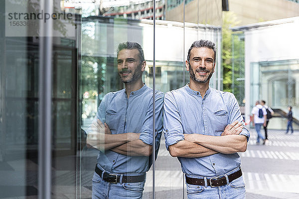 Lächelnder Geschäftsmann mit Spiegelung auf einer Glasfassade  Berlin  Deutschland