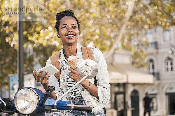 Glückliche junge Frau mit Motorroller beim Eisessen in der Stadt  Lissabon  Portugal