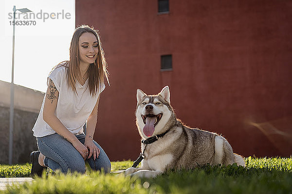 Porträt einer glücklichen jungen Frau auf einer Wiese mit ihrem Hund am Abend