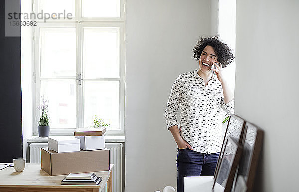 Lachende junge Frau am Telefon im Home-Office