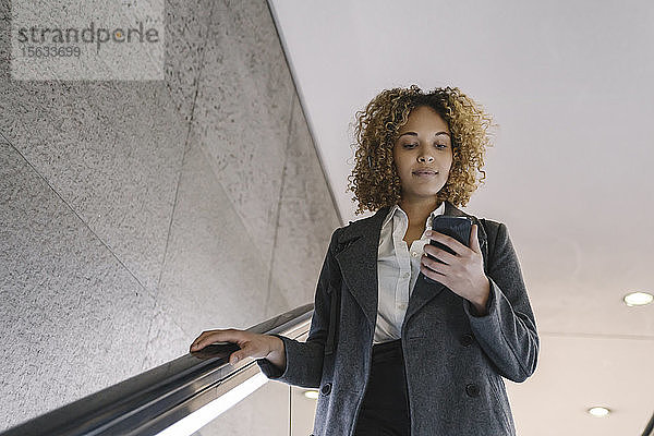 Frau benutzt Handy auf Rolltreppe