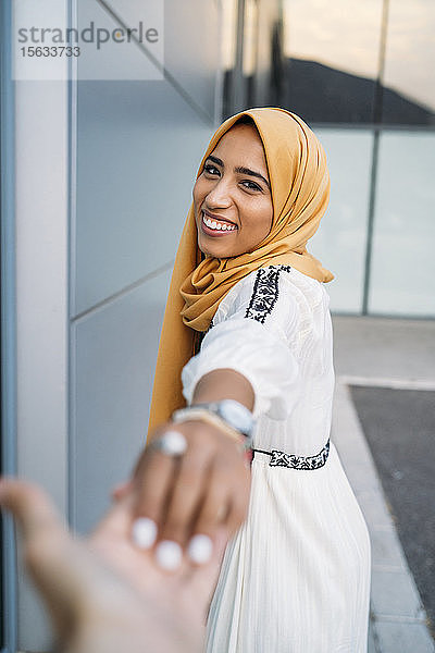 Junge muslimische Frau lächelt und nimmt die Hand eines Mannes  der einen Hidschab trägt
