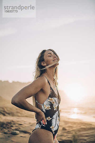 Junge blonde Frau im Badeanzug bei Sonnenaufgang am Strand