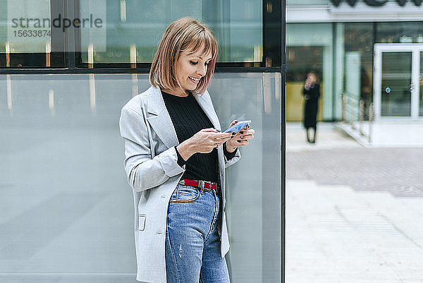 Lächelnde Frau benutzt Handy im Glasgebäude