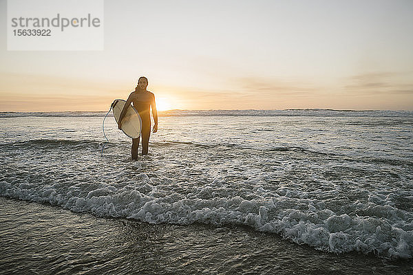 Surfer mit Surfbrett im Meer während des Sonnenuntergangs