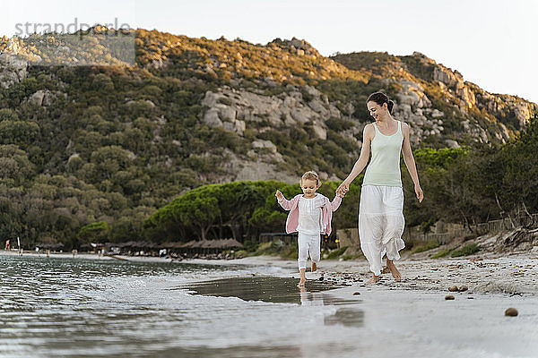 Glückliche Mutter geht mit Tochter am Strand spazieren