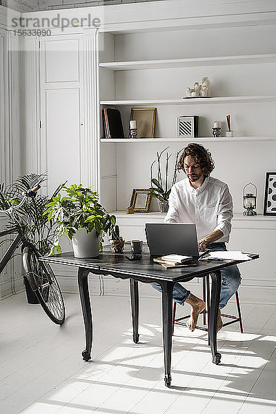 Mann sitzt zu Hause am Tisch mit Laptop