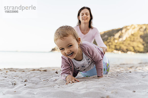 Porträt eines glücklichen kleinen Mädchens  das mit dem Earth-Beachball spielt  während seine Mutter im Hintergrund sitzt