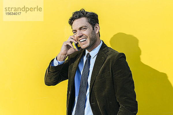 Glücklicher Geschäftsmann am Telefon vor der gelben Wand