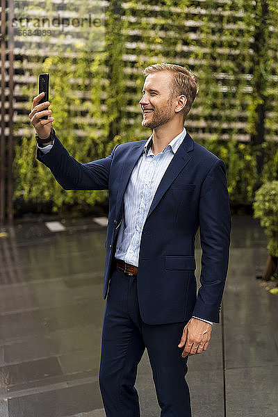 Junger Geschäftsmann nimmt während eines regnerischen Tages in Bangkok einen Selfie mit Smartphone