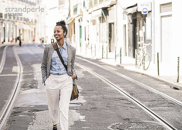 Lächelnde junge Frau mit drahtlosen Kopfhörern in der Stadt unterwegs  Lissabon  Portugal