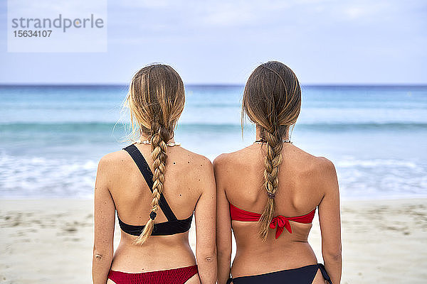Rückansicht von zwei jungen Frauen  die am Strand stehen
