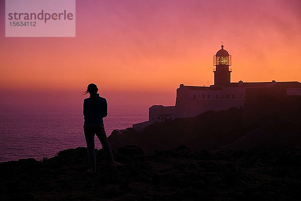 Portugal  Algarve  Silhouette einer Person  die im Morgengrauen das Meer bewundert  mit dem Leuchtturm von Cape Saint Vincent im Hintergrund