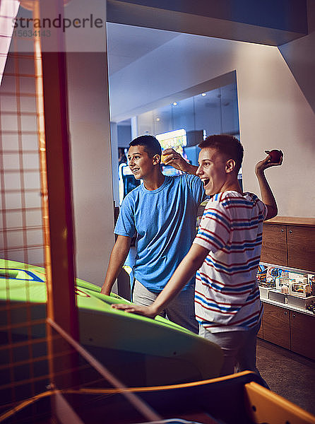 Glückliche Teenager-Freunde  die in einer Spielhalle Bälle auf einen Spielautomaten werfen