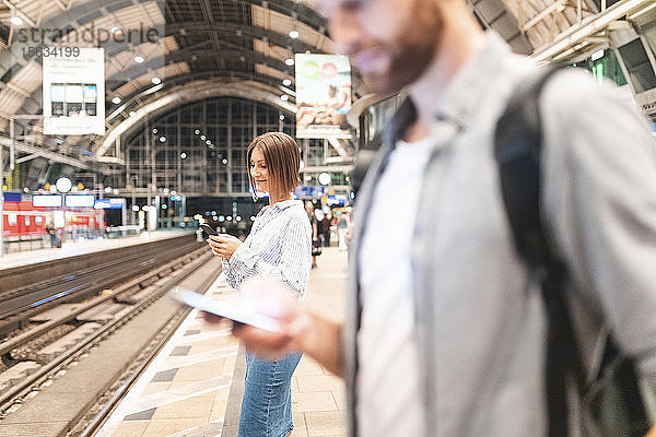 Menschen  die am Bahnhof auf den Zug warten und Smartphones benutzen  Berlin  Deutschland