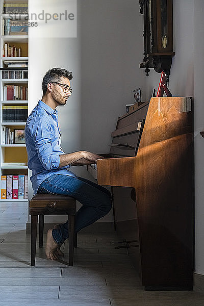 Barfüssiger junger Mann spielt zu Hause Klavier