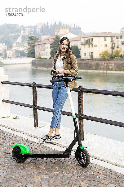 Junge Frau mietet einen E-Scooter und hält ihr Smartphone in Verona  Italien