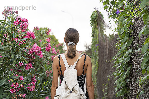 Rückenansicht einer jungen Frau mit Rucksack beim Spaziergang in einem Park