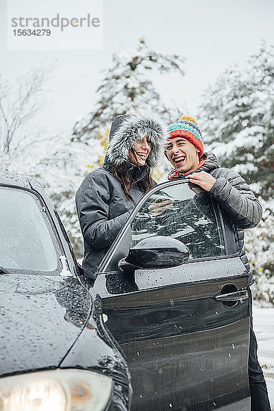 Lachendes junges Paar mit Auto im Winterwald