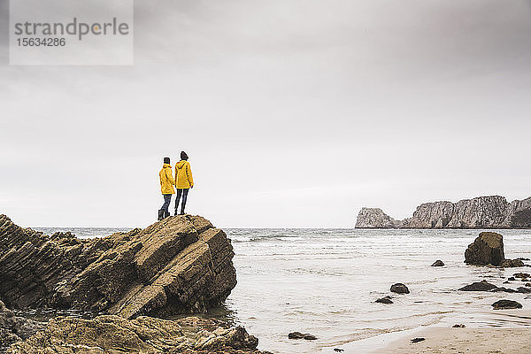 Junge Frau in gelben Regenjacken und auf einem Felsen am Strand stehend  Bretagne  Frankreich