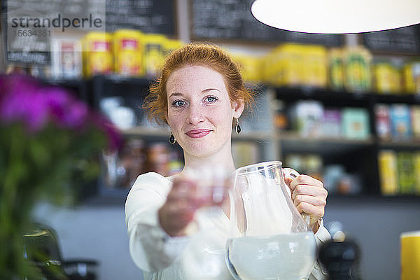 Junge Frau  die im Café arbeitet und ein Wasserglas schenkt