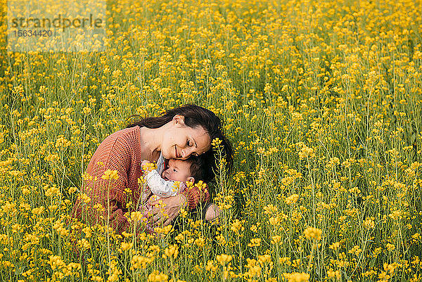 Glückliche Mutter kuschelt mit Mädchen in einem Rapsfeld