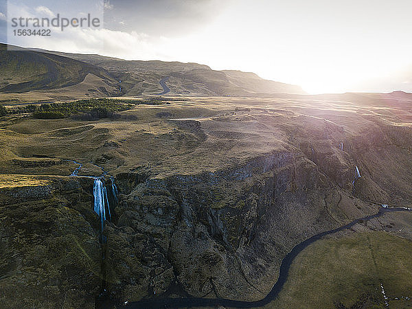 Island  Luftaufnahme eines Wasserfalls  der bei Sonnenuntergang von einer hohen Klippe herunterplätschert