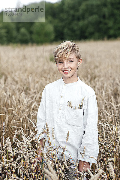 Porträt eines glücklichen blonden Jungen  der in einem Haferfeld steht
